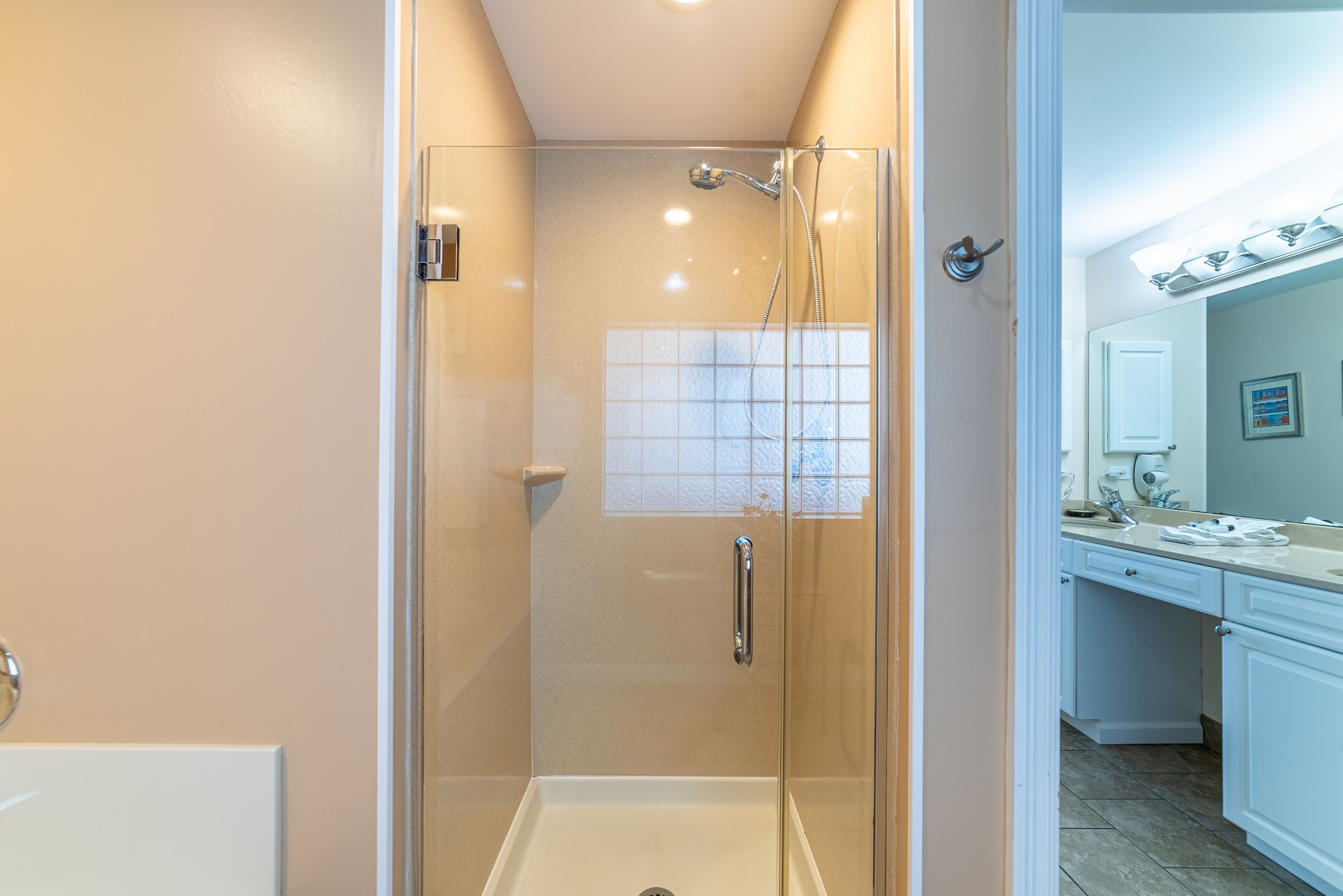 Une douche fermée par des parois de verre, avec une baignoire blanche, un lavabo blanc et un miroir au-dessus du lavabo.