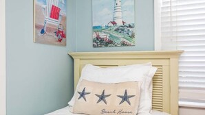 A bedroom with a bed, a headboard, and two wall art pieces depicting a beach chair and a lighthouse. - Little House | Pet Friendly Cottage + Easy Walk to the Sand! (Tybee Island)