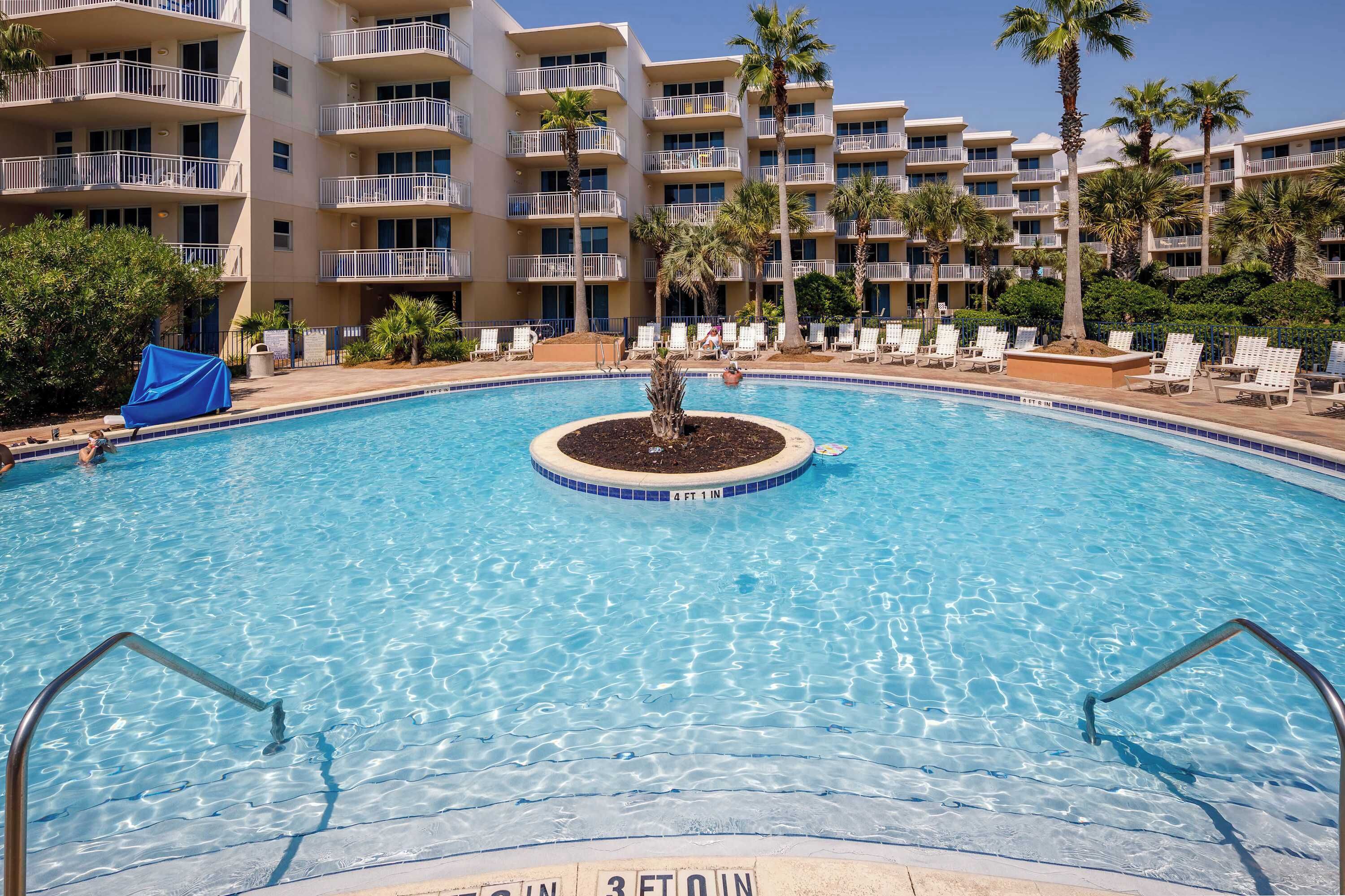 Ein Swimmingpool mit einer zentralen Insel, umgeben von Liegestühlen und Palmen.