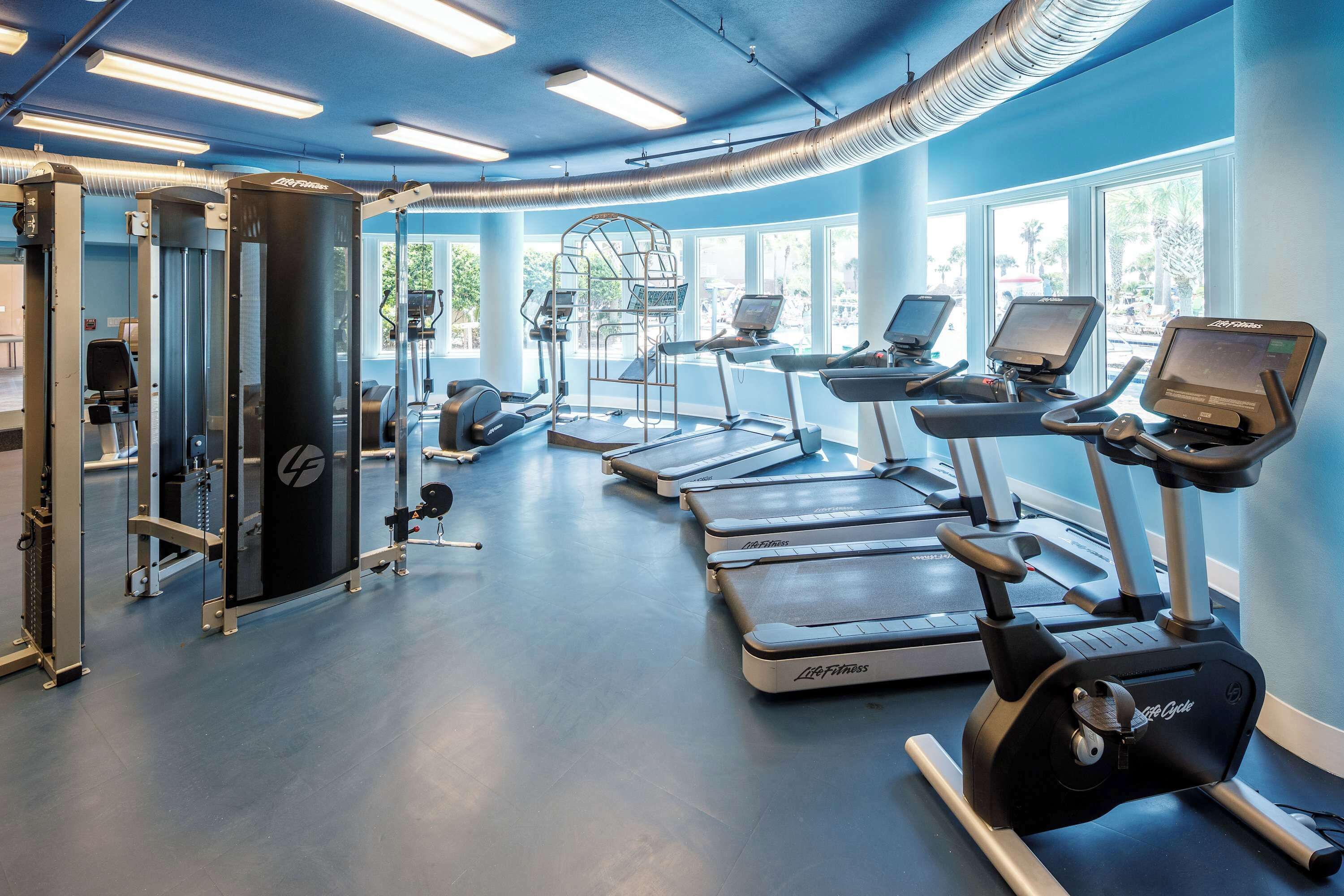 Une salle de sport équipée de machines de cardio, de matériel d’entraînement en force et dotée de grandes fenêtres.