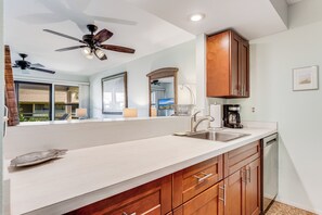 A kitchen with a white countertop, wooden cabinets, a ceiling fan, and a dishwasher.