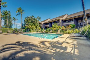 A swimming pool with lounge chairs, palm trees, and a building with balconies.