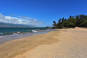 A beach with clear skies, calm waters, and a distant mountain range.