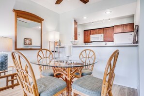Un comedor con una mesa de vidrio rodeada de sillas de mimbre, una cocina con armarios de madera y un espejo grande en la pared.