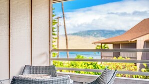 Un balcone con sedie in vimini, vista su vegetazione e un edificio sullo sfondo.