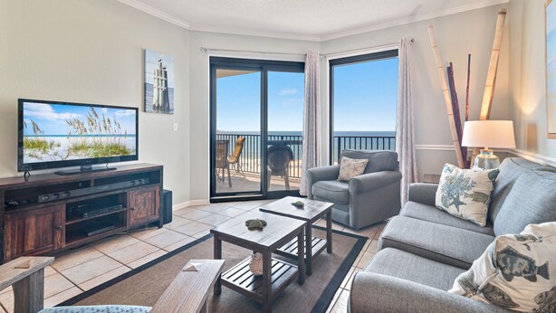 A living room with a television, sofa, coffee table, and a view of the ocean.