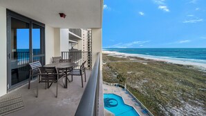 Un balcon avec une table et des chaises, donnant sur une plage et une piscine.