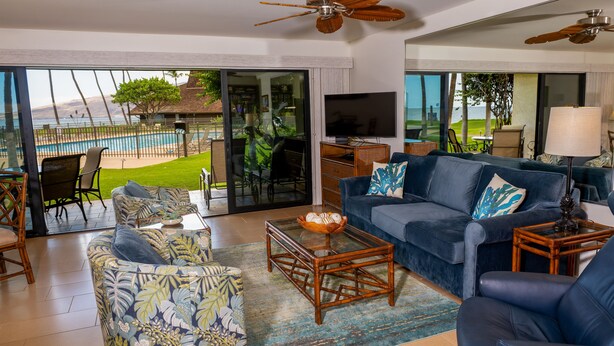 A living room with a sofa, armchairs, a coffee table, and a TV. There is a view of a pool and a patio outside. - Ma'alaea Surf Unit E3-1 BR Ground Floor Beachfront Condo, Wi-Fi, AC, Pool, TV (Kihei)