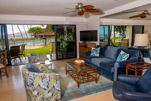 A living room with a sofa, armchairs, a coffee table, and a TV. There is a view of a pool and a patio outside. - Ma'alaea Surf Unit E3-1 BR Ground Floor Beachfront Condo, Wi-Fi, AC, Pool, TV (Kihei)