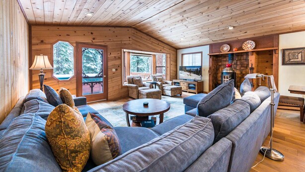 Ein gemütliches Blockhaushaus-Interieur mit Holzbalkendecke, einer großen Couch, einem Fernseher und einem Kamin.