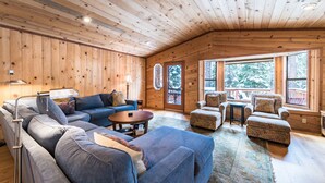 Ein gemütliches Blockhauss-Interieur mit Holzbalkendecke, großem Fenster und einer Sitzecke mit Sofa und Sesseln.