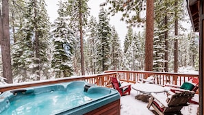Ein Whirlpool auf einer Holzterrasse, umgeben von schneebedeckten Bäumen.