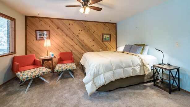 A bedroom with a bed, a ceiling fan, a nightstand, a lamp, and a chair.