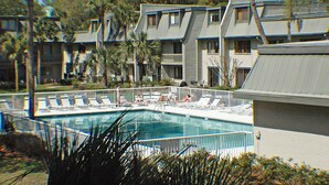 Ein Swimmingpool, umgeben von Liegestühlen und Palmen, mit einem mehrstöckigen Gebäude im Hintergrund.