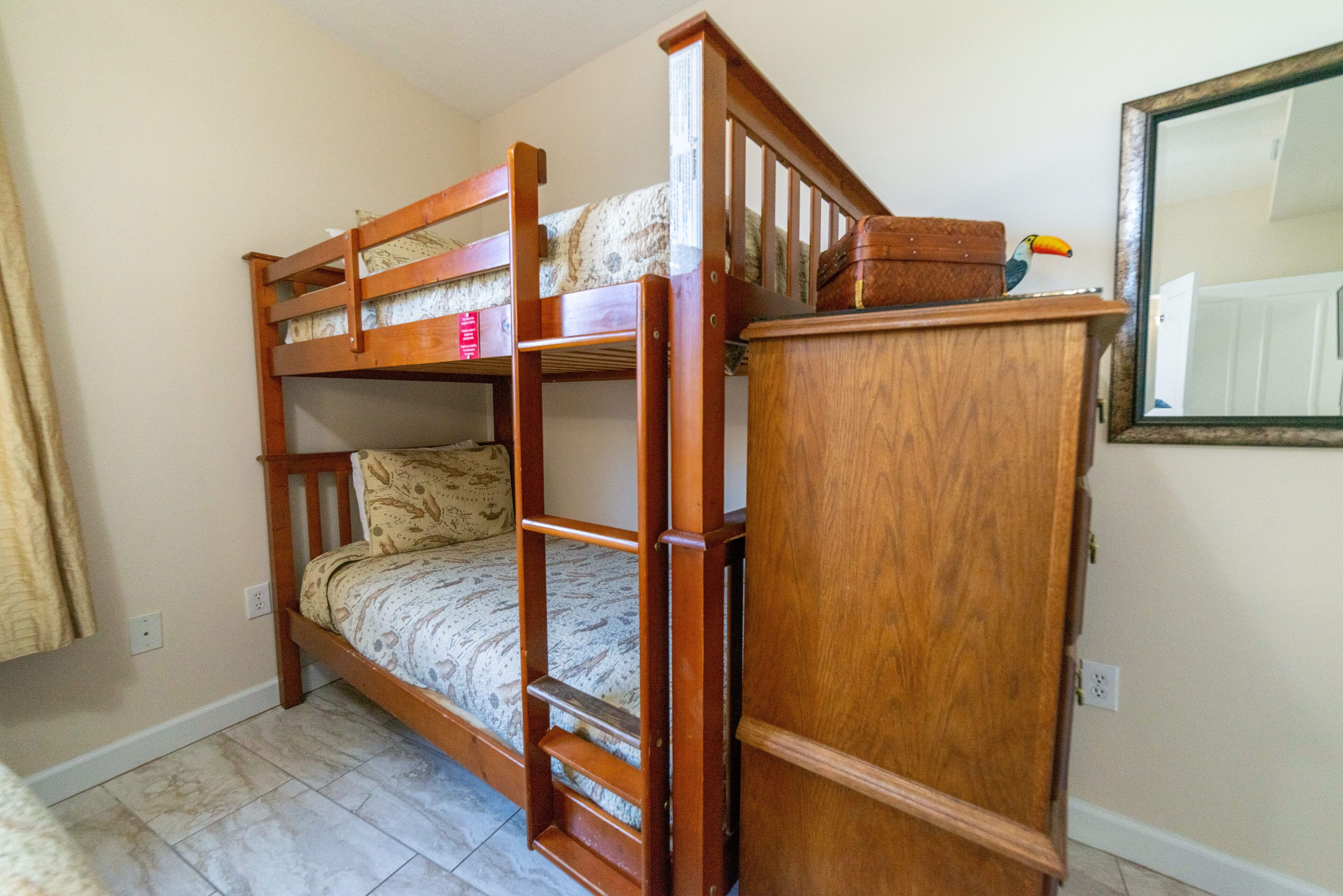 Una cama litera con escalera, un armario de madera y un espejo en la pared.