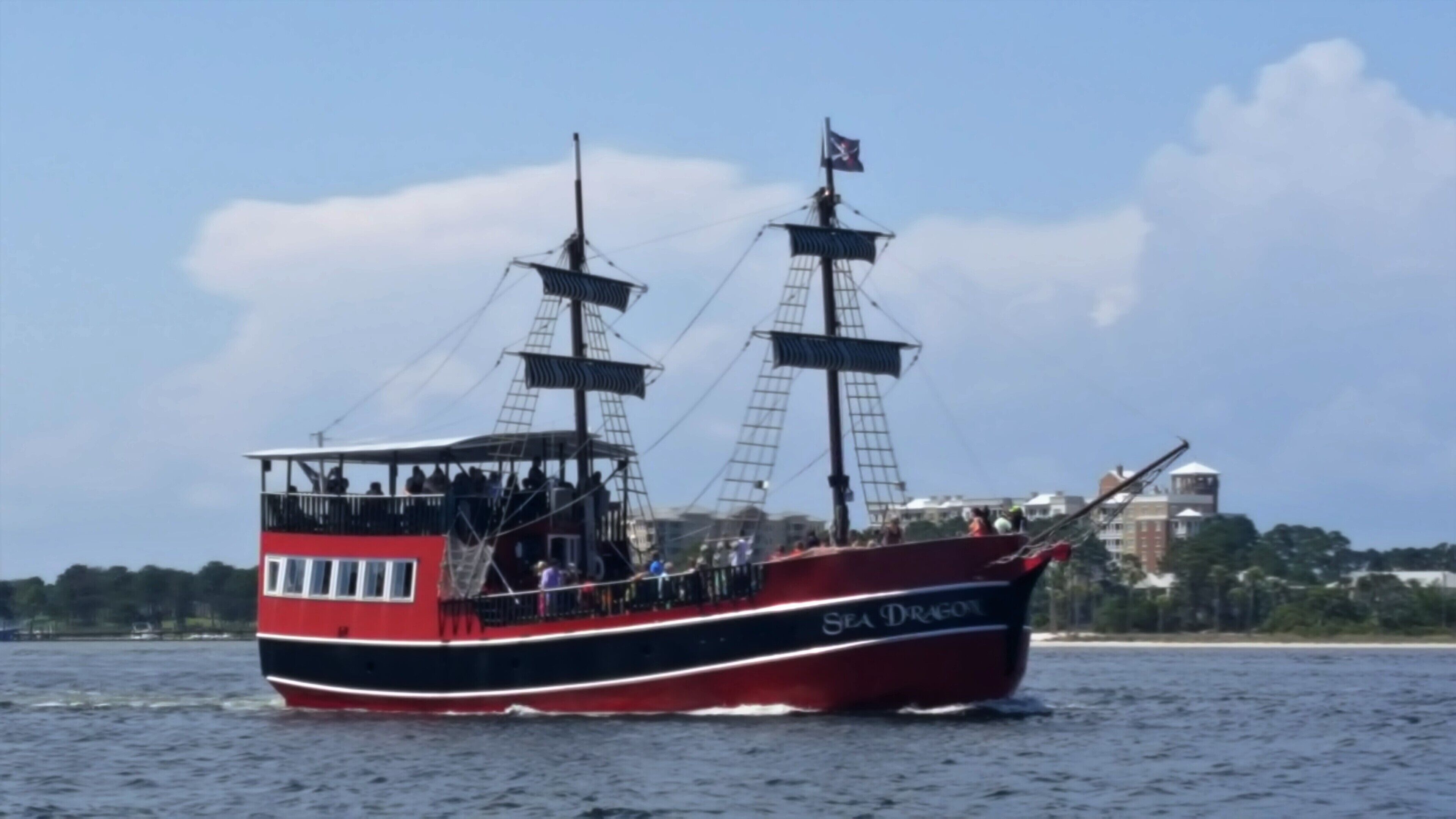 Un navire rouge et noir, nommé Sea Dragon, avec un pavillon hissé, naviguant sur l’eau.