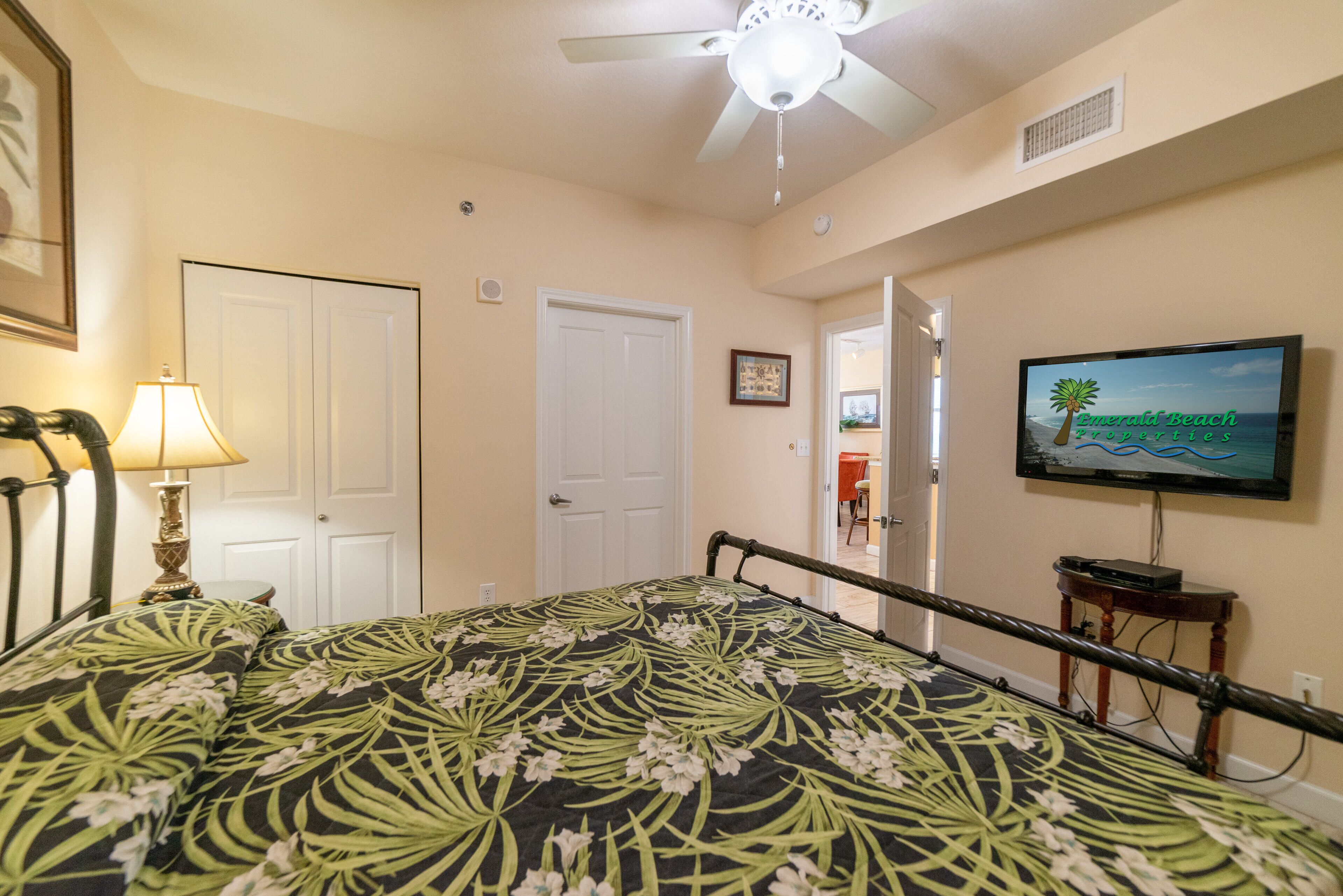 A bedroom with a bed, a ceiling fan, a TV, and a door.
