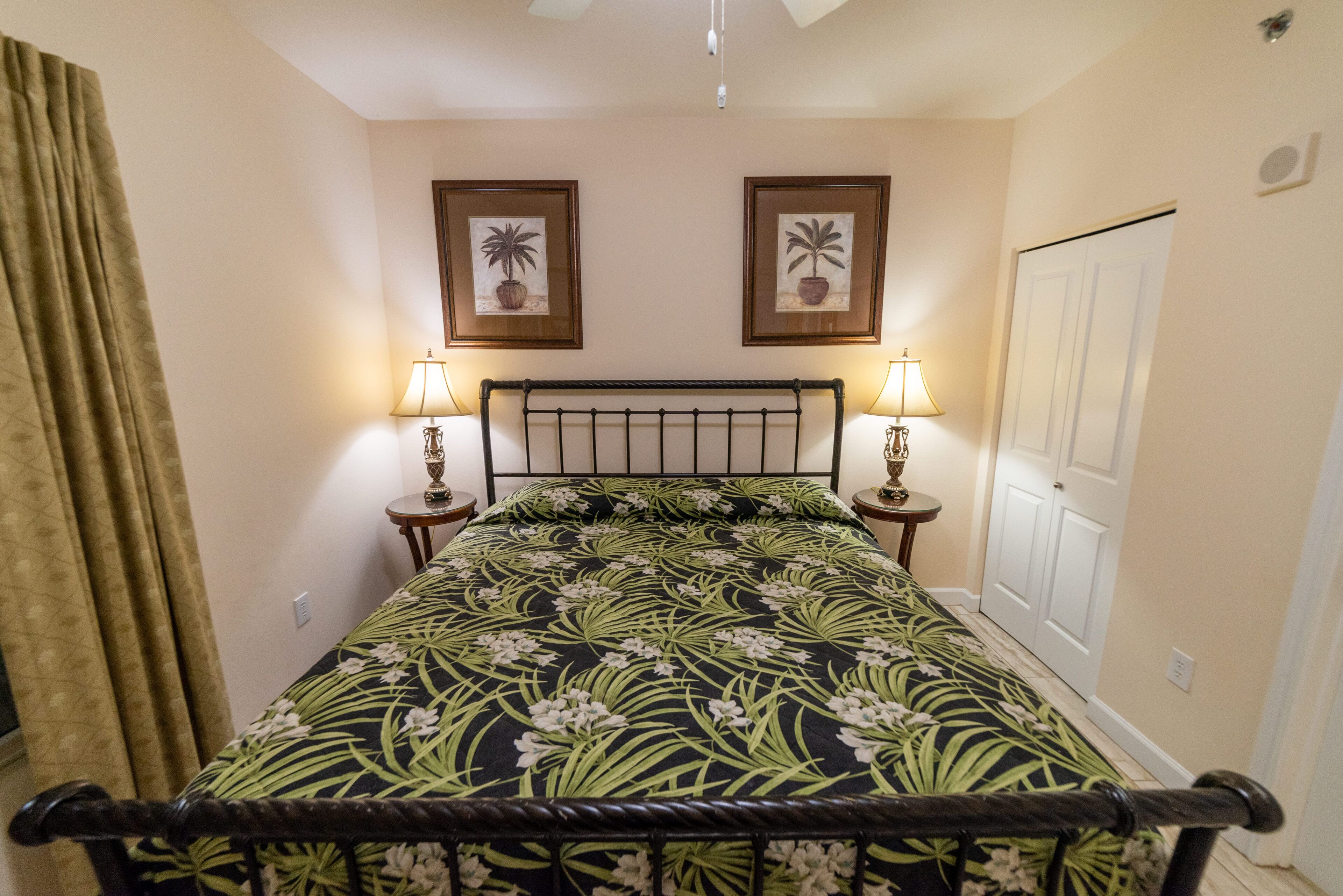 A bedroom with a bed, two bedside lamps, a door, and two framed pictures on the wall.
