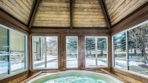 A wooden interior with a large windowed area, a hot tub, and a view of a snowy outdoor area. - Canyons View 20: 2 bed 2 bath, walk to the lift (Park City)