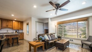A spacious living area with a large window, a ceiling fan, and a wooden floor. - Canyons View 20: 2 bed 2 bath, walk to the lift (Park City)