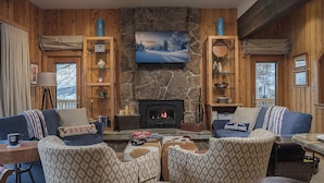 A cozy living room with a stone fireplace, wooden walls, and a television mounted above it. There are two sofas and a coffee table in the center. - Luxury + Pool/Hot Tub + Ski in/Ski out - Right-O-Way Chalet (Steamboat Springs)