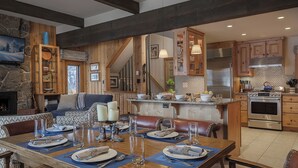 A spacious dining area with a large wooden table set for a meal, a fireplace, and a kitchen with modern appliances. - Luxury + Pool/Hot Tub + Ski in/Ski out - Right-O-Way Chalet (Steamboat Springs)