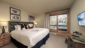 A bedroom with a large bed, a desk, a chair, a window with a view of trees, and framed pictures on the wall. - Luxury + Pool/Hot Tub + Ski in/Ski out - Right-O-Way Chalet (Steamboat Springs)
