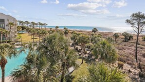 Een resort met een zwembad, palmbomen en uitzicht op het strand.
