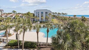 Een resort met een groot zwembad, palmbomen en uitzicht op het strand.