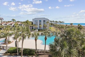 A resort with a large pool, palm trees, and a view of the beach.