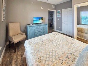 Une chambre à coucher avec un lit, une commode, une chaise et un téléviseur.
