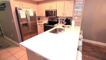 A modern kitchen with stainless steel appliances, white cabinetry, and a wooden floor.