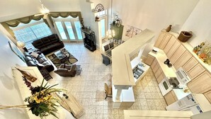 A spacious living area with a sofa, coffee table, and decorative plants. A kitchen area with modern appliances and wooden cabinets is visible. - Villa close to beach Includes 6-Seat Golf Cart! 5257 TS (Miramar Beach)
