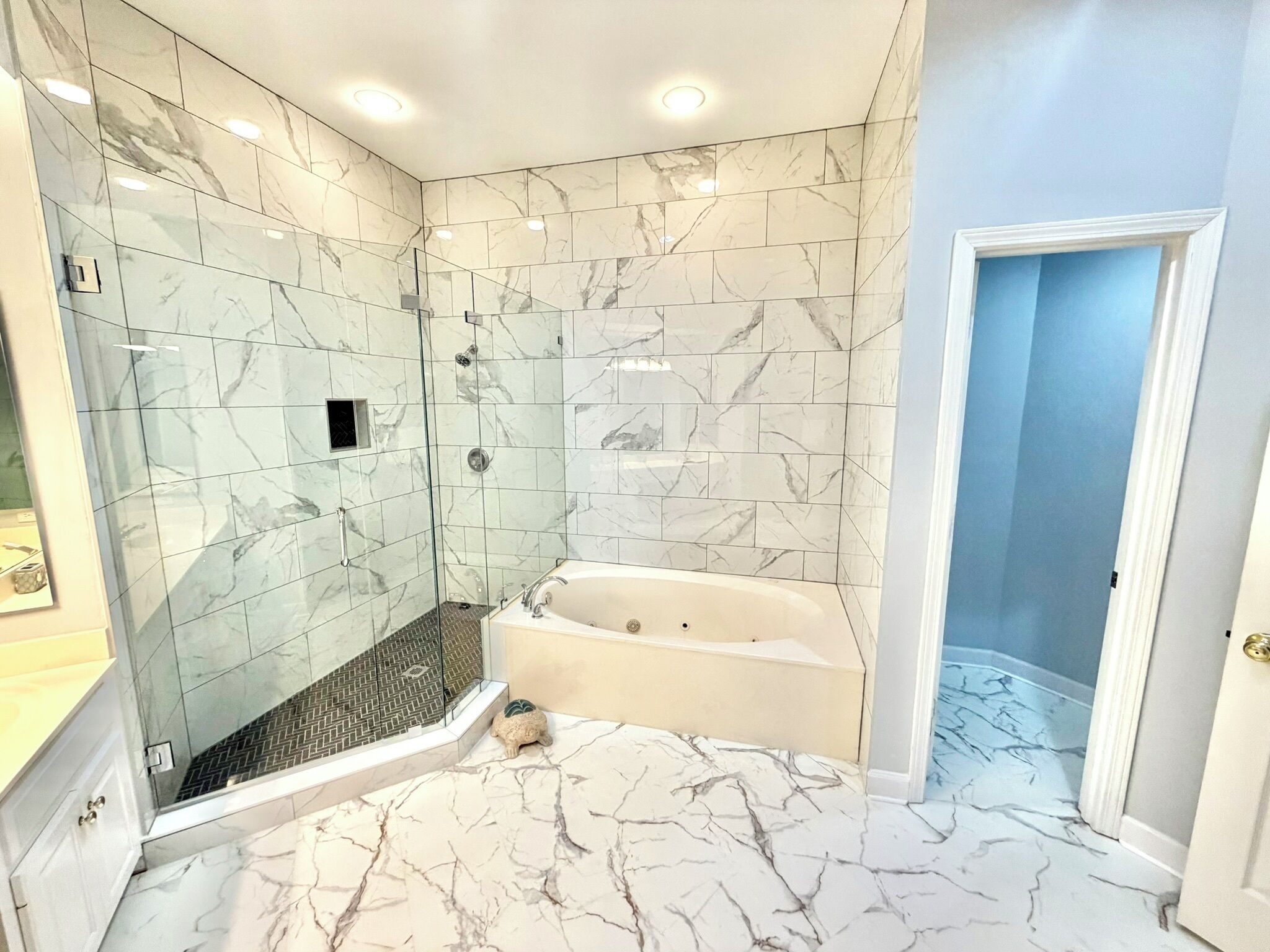 A bathroom with a glass-enclosed shower, a bathtub, and marble flooring.