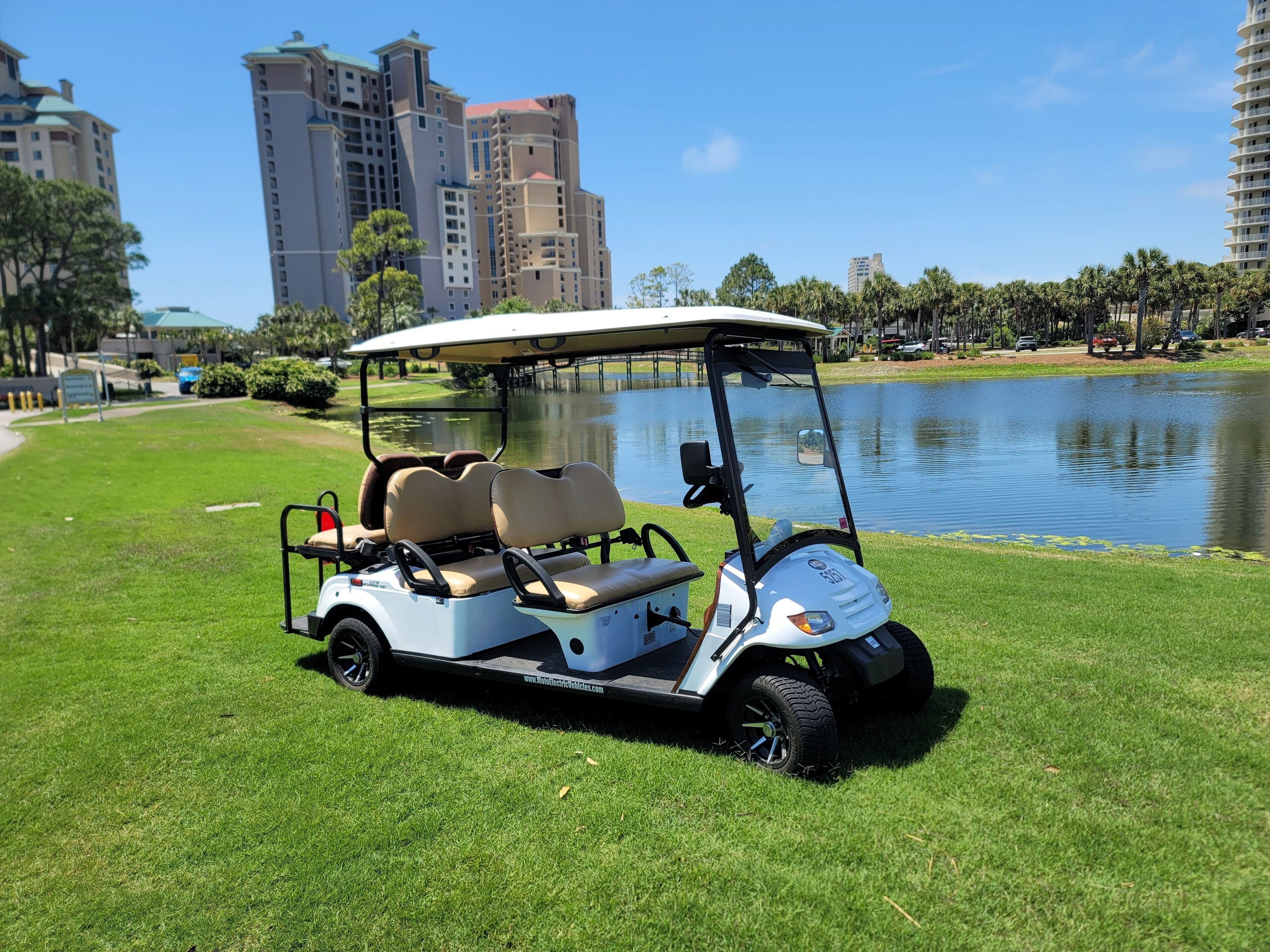 A golf cart parked on a grassy area near a body of water with buildings in the background.