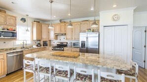 A modern kitchen with wooden cabinets, stainless steel appliances, and a large island with bar stools. - Fabulous Gulf Front Home, Gated neighborhood, Double porches, Santa Rosa Beach (Santa Rosa Beach)