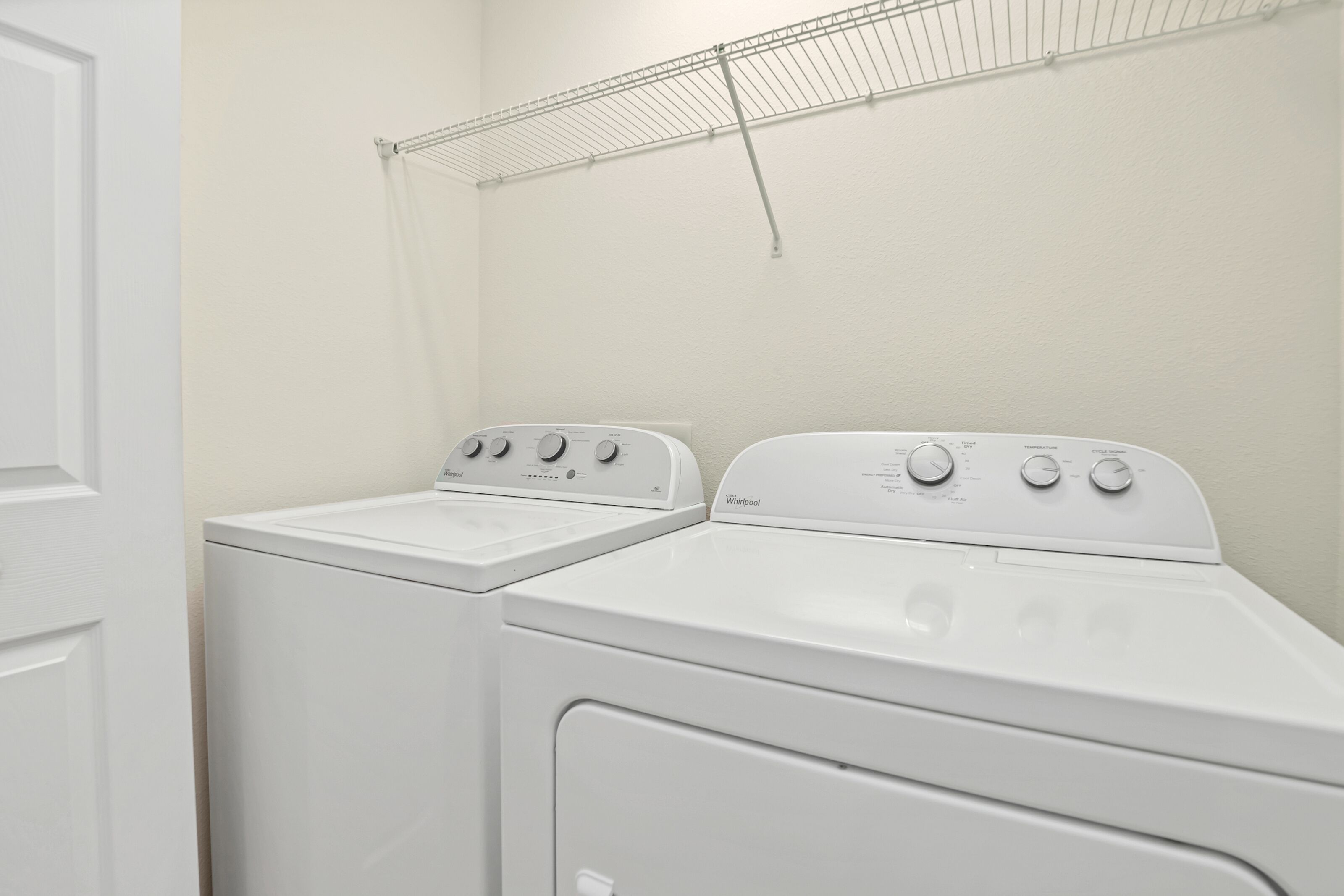 Un lavadero con dos lavadoras y secadoras Whirlpool blancas, un tendedero metálico en la pared y una puerta blanca.