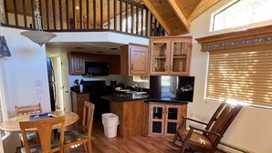 Et rummeligt køkken med træskabe, et spiseområde med bord og stole, et indbygget tv og en trappe, der fører til en etage ovenpå.
