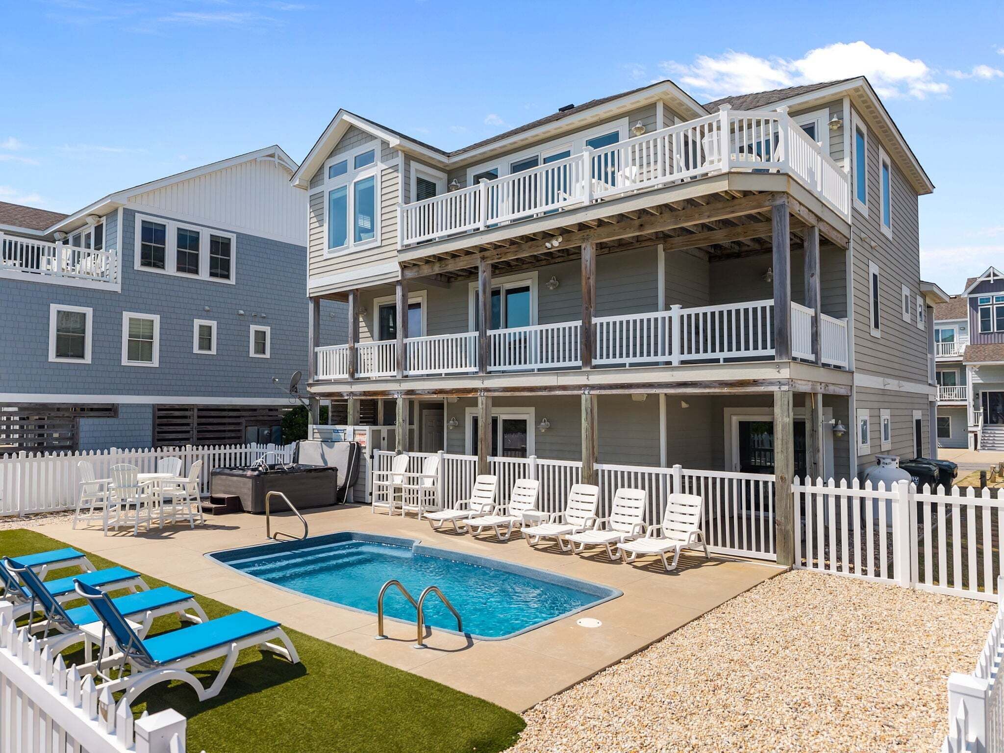 A multi-story building with a pool, outdoor seating, and a white picket fence.