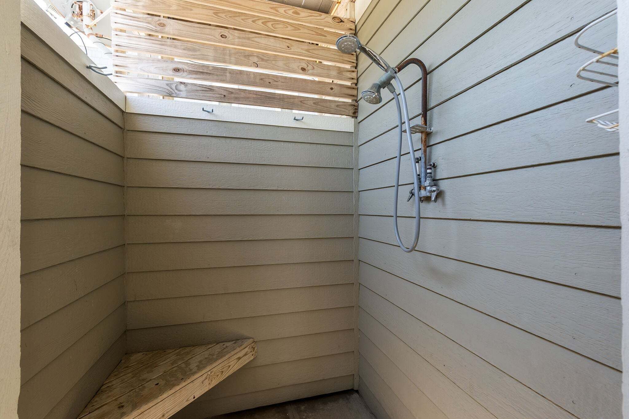 Un petit espace douche fermé, avec des lambris en bois au plafond et un pommeau de douche en métal.