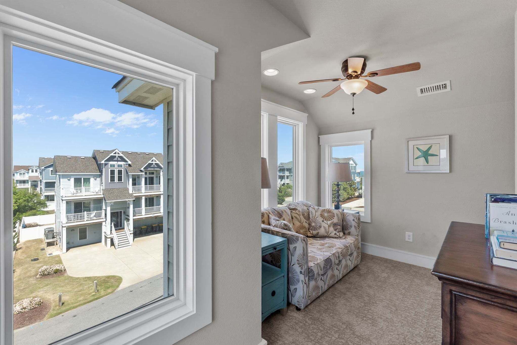 A room with a large window, a ceiling fan, a sofa, and a small table.