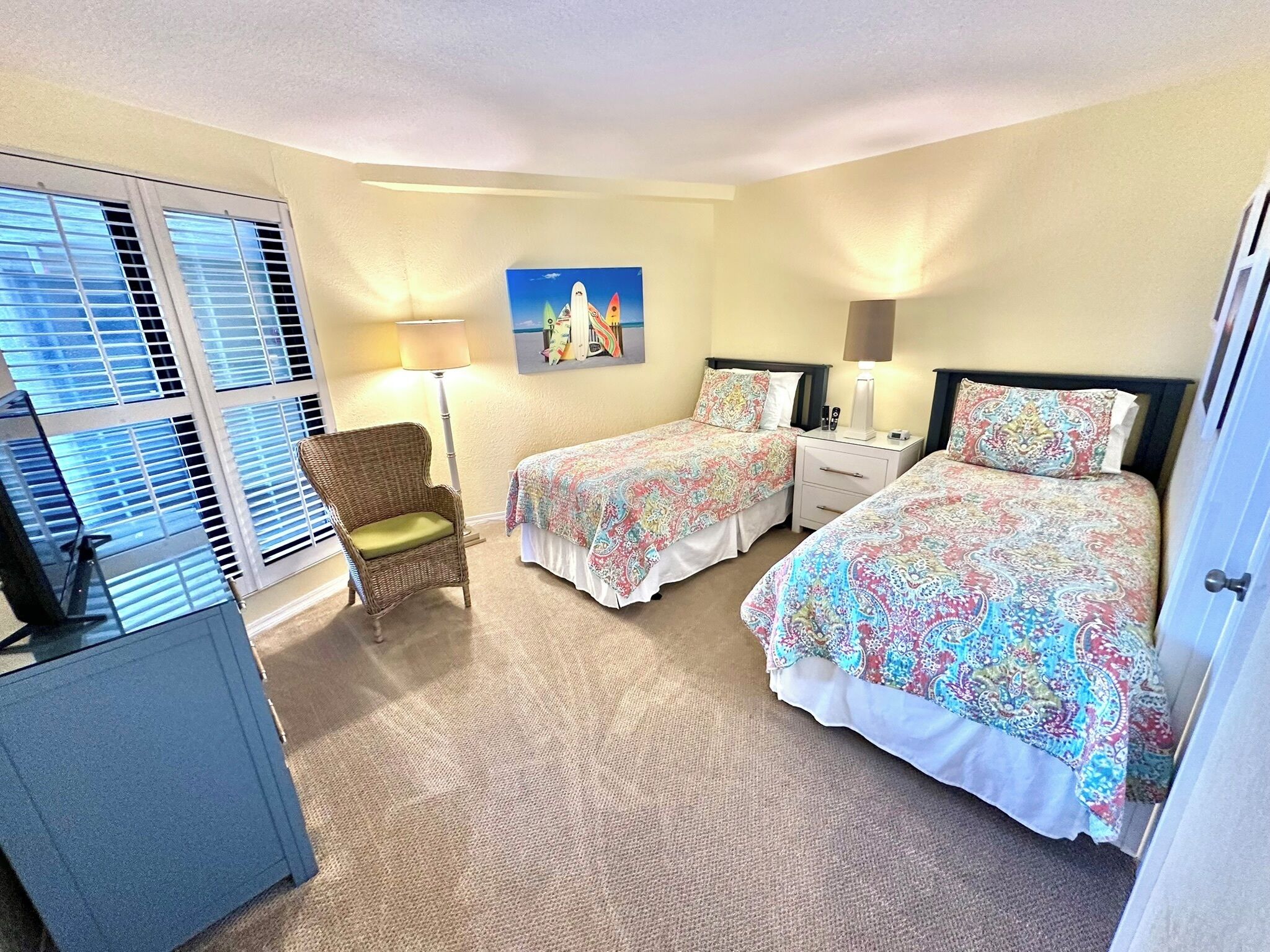 A hotel room with two beds, a chair, a desk, and a painting on the wall.