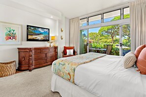 Ein geräumiges Schlafzimmer mit einem großen Bett, einer hölzernen Kommode, einem Fernseher und Blick auf eine tropische Landschaft durch das Fenster.