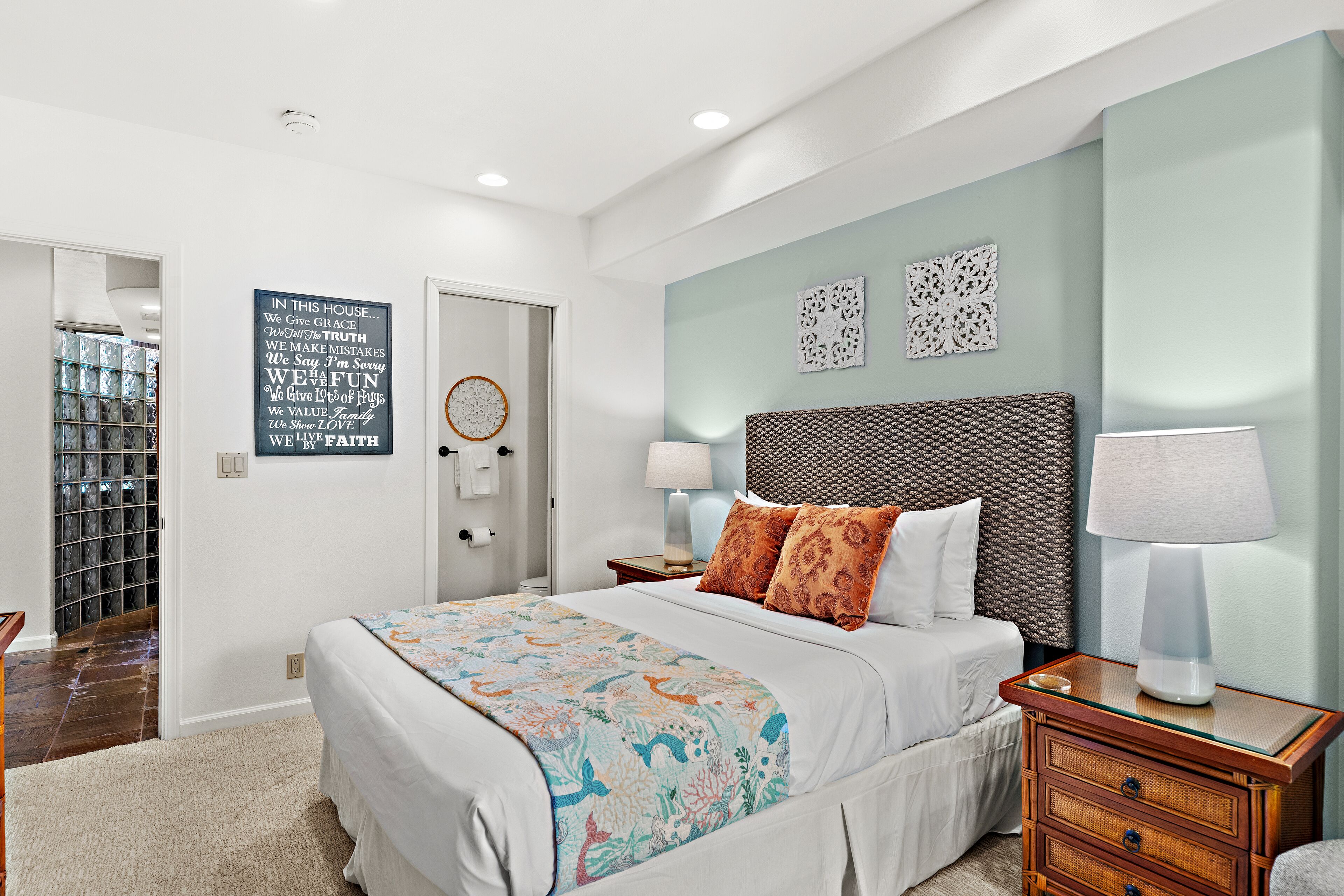 A bedroom with a large bed, a bedside table with a lamp, a wall with decorative items, and a closet with glass doors.