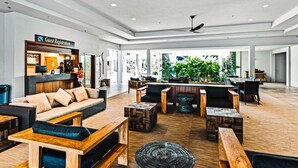 Un hall d’entrée spacieux avec un comptoir d’enregistrement, des coins salon confortables et une grande plante au centre.