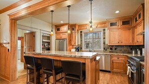 Une cuisine spacieuse avec des meubles en bois, un grand îlot central doté de tabourets, des appareils en acier inoxydable et un éclairage suspendu.