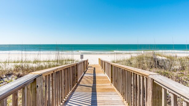 Een houten looppad dat naar een strand leidt, onder heldere luchten.