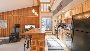 Una cocina moderna con armarios de madera, una isla central con taburetes, un refrigerador negro y una estufa a leña.
