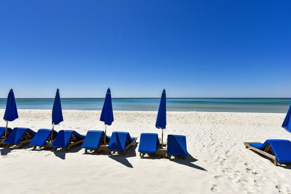 Een strand met rijen blauwe ligbedden en bijpassende parasols, uitgestald aan de zandkust.