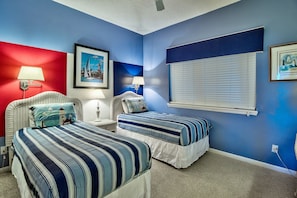 A bedroom with two beds, a red accent wall, and a large window with blinds.